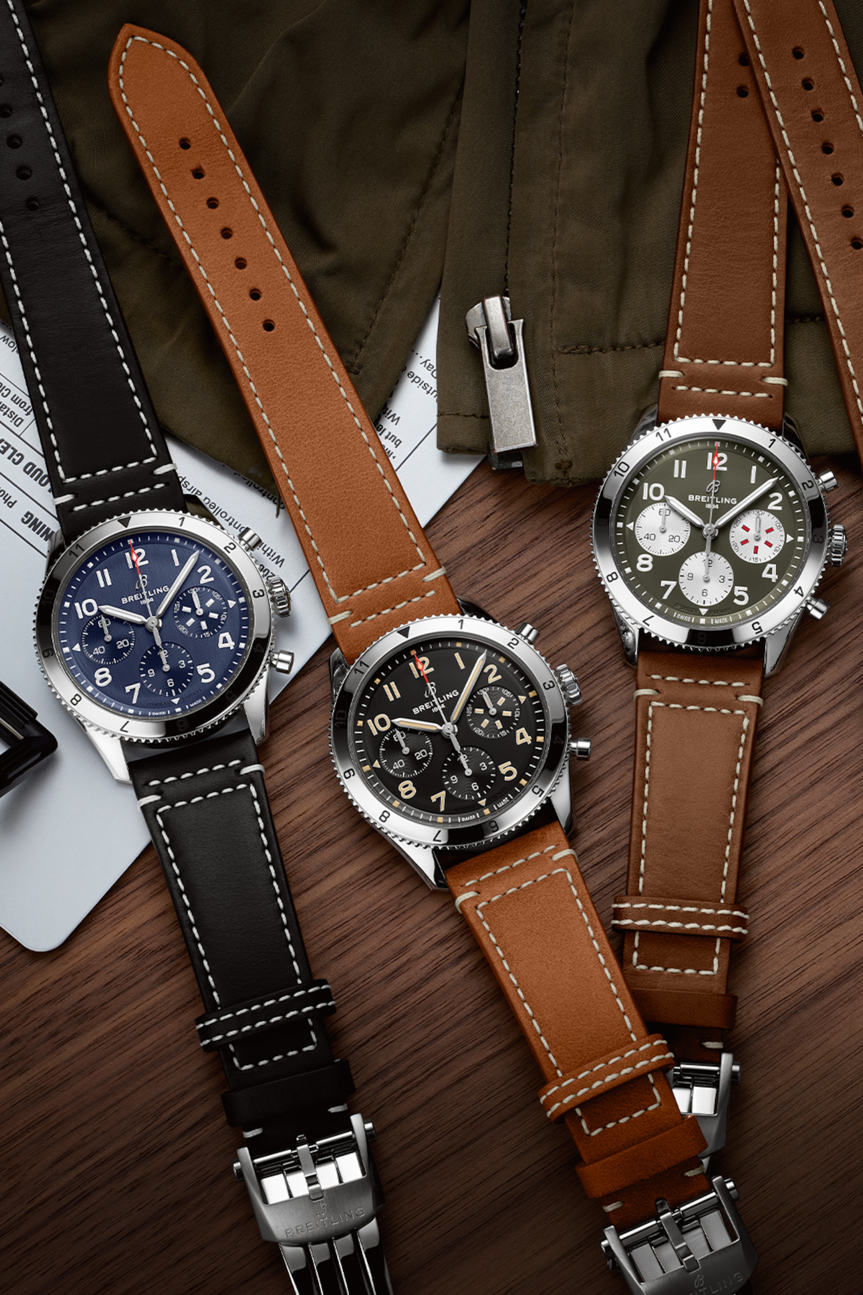 Three Classic AVI with different colored, dark leather straps on a dark brown table.