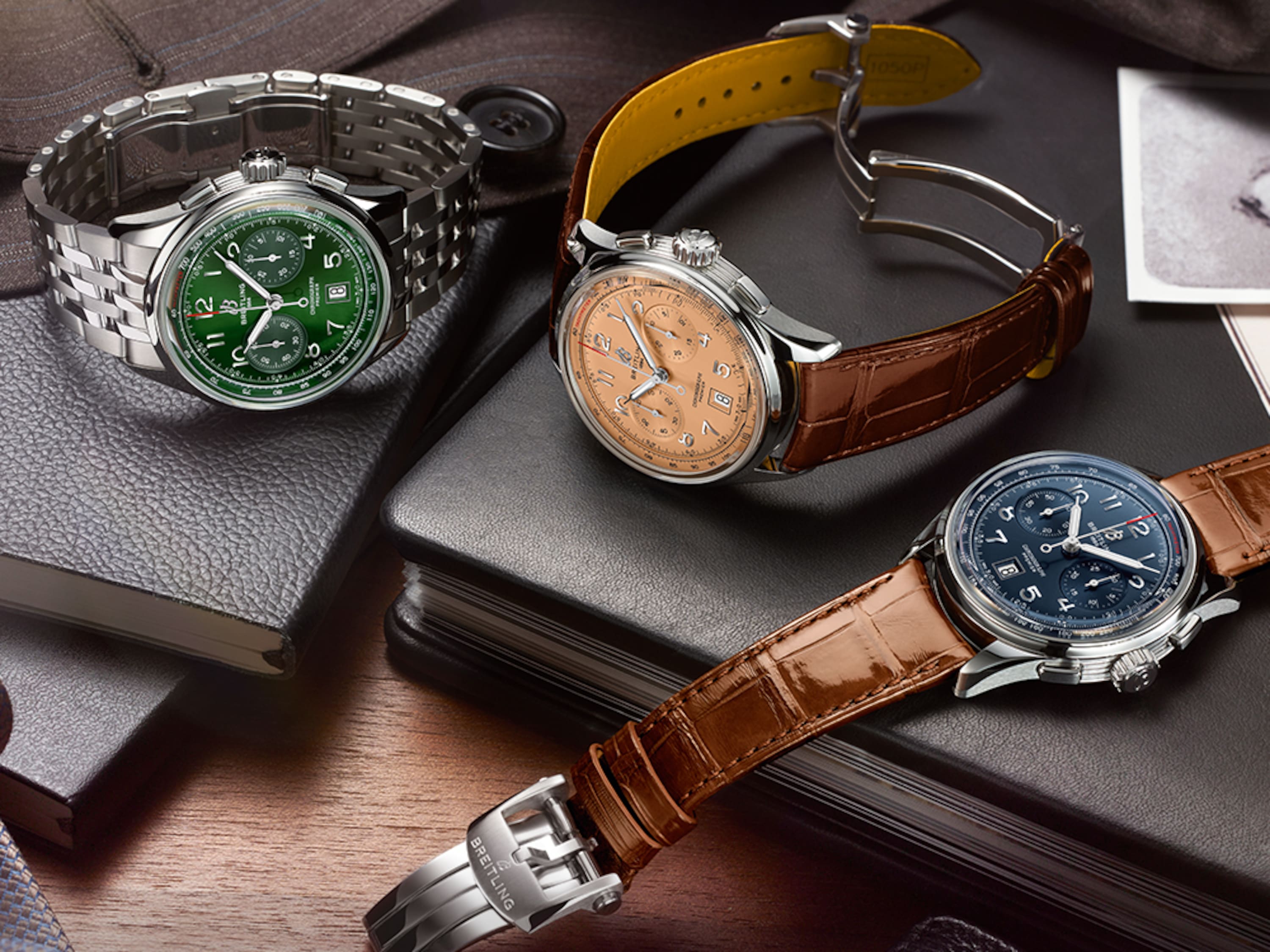 Three Premier watches with elegant bracelets lie on black notebooks on a brown table.